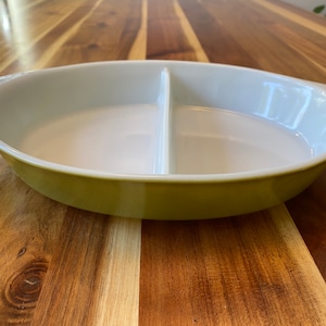 May include: An oval, divided serving dish. The exterior is light green, and the interior is white. A vertical divider splits the dish into two sections. It has handles at each end. Likely made of ceramic or glass.
