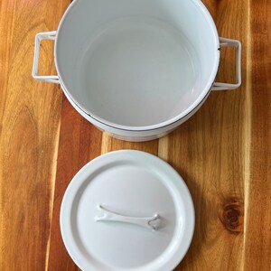 Puede incluir: Olla de esmalte blanco con tapa blanca y un asa a cada lado. La olla y la tapa tienen un dise&ntilde;o sencillo.
