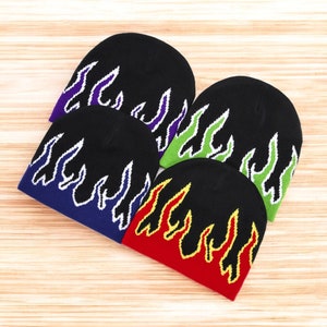 Puede incluir: Cuatro gorros de punto negros con dise&ntilde;os de llamas en diferentes colores. Los gorros tienen contornos blancos alrededor de las llamas. Los colores de las llamas son morado, verde, azul y rojo.