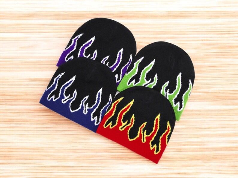 Puede incluir: Cuatro gorros de punto negros con dise&ntilde;os de llamas en diferentes colores. Los gorros tienen contornos blancos alrededor de las llamas. Los colores de las llamas son morado, verde, azul y rojo.