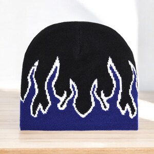 Puede incluir: Gorro negro con un dise&ntilde;o de llamas azules y blancas.