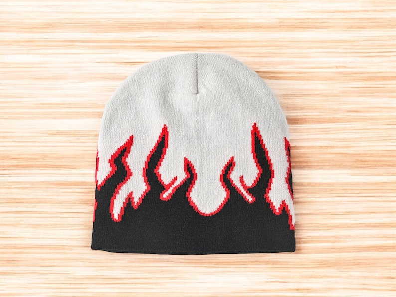 Puede incluir: Un gorro gris con un dise&ntilde;o de llamas negras y rojas. El gorro est&aacute; hecho de un tejido suave y de punto.
