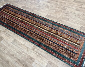 Könnte beinhalten: Ein langer, rechteckiger Teppich mit Streifenmuster in den Farbtönen Türkis, Rot, Braun und Gold. Der Teppich hat einen Rand und Fransen an einem Ende. Das Design zeigt geometrische und florale Motive und schafft eine traditionelle Ästhetik.