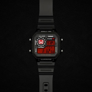 Può includere: Un orologio da polso digitale nero con cassa quadrata, cinturino in resina nera e display rosso. Il quadrante mostra il logo Honda, la scritta Casio Type R, World Time e Illuminator. Lo schermo digitale indica l'ora 1:12:56 in rosso.