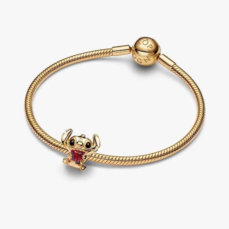 Pode incluir: Pulseira dourada com um berloque com Stitch segurando um cora&ccedil;&atilde;o vermelho. A pulseira tem um design de corrente de cobra e um fecho redondo. O berloque &eacute; detalhado com olhos pretos e um cora&ccedil;&atilde;o vermelho.