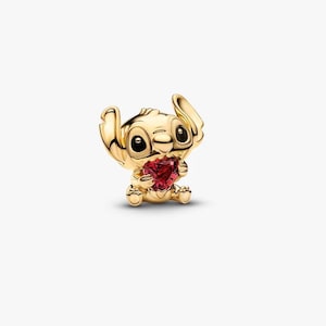 Pode incluir: Um berloque dourado com o personagem Stitch de Lilo & Stitch. Stitch est&aacute; segurando uma pedra preciosa vermelha em forma de cora&ccedil;&atilde;o. O berloque tem detalhes e est&aacute; em um fundo branco.