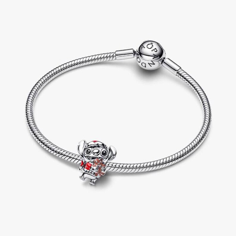 Op de afbeelding: Een zilveren armband met een Stitch-bedel. De bedel heeft rode en bruine details. De armband heeft een ronde sluiting met de letters "PANDORA".
