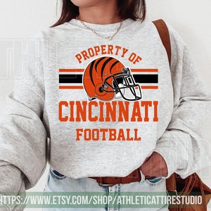 May include: A gray sweatshirt with the text "PROPERTY OF CINCINNATI FOOTBALL" and a black and orange football helmet graphic.