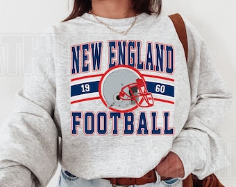 May include: A light gray sweatshirt with the words "NEW ENGLAND FOOTBALL" in navy blue and red lettering. A football helmet graphic is centered between the words. The numbers "19" and "60" are above and below the helmet.