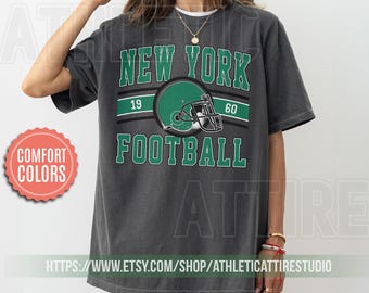 May include: A gray t-shirt with a green and white graphic that says "New York Football" with a football helmet in the center. The numbers 19 and 60 are on either side of the helmet.