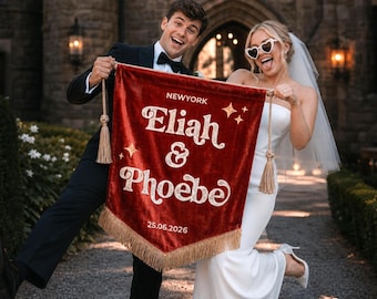 May include: A deep red velvet pennant banner featuring gold embroidered text that reads NEWYORK, Eliah & Phoebe, and 25.06.2026. The banner is decorated with gold star accents, gold tassels on the top corners, and gold fringe along the bottom edge.