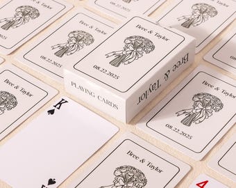 May include: A white playing card box and cards with a floral bouquet design. The cards and box have the text "Bree & Taylor" and the date "08.22.2025". The King of Spades and the Four of Diamonds are visible.