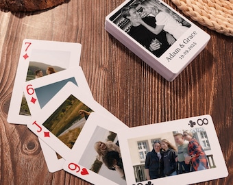 May include: A deck of playing cards with personalized photos. The top card of the deck has the text "Adam & Grace 19.09.2025". Several cards are fanned out, displaying photos and card values. The background is a dark wood surface.
