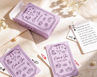 Puede incluir: Una baraja de cartas personalizada en una caja de color morado claro con los nombres Cala & Joe, la fecha 12/07/2025 e ilustraciones de iconos de boda. Las cartas muestran diseños morados a juego y un mensaje impreso de felicitación.