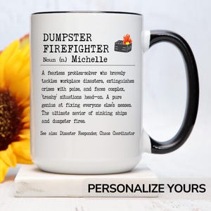 May include: White ceramic mug with a black handle. The mug has a black and white design that reads "DUMPSTER FIREFIGHTER Noun (n.) Michelle A fearless problem-solver who bravely tackles workplace disasters, extinguishes crises with poise, and faces complex, trashy situations head-on. A pure genius at fixing everyone else's messes. The ultimate savior of sinking ships and dumpster fires. See also Disaster Responder, Chaos Coordinator"