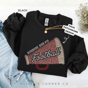 May include: A black crewneck sweatshirt featuring a graphic of a megaphone with a red and white gingham pattern. The text RIVERSIDE HIGH #34 and Football is printed on the megaphone. The design includes a faux patchwork effect.