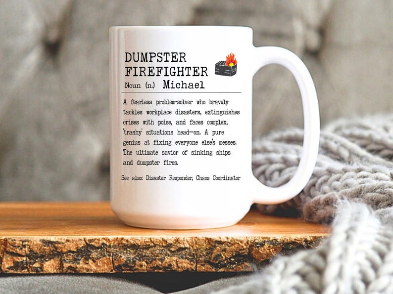 May include: White ceramic mug with a black and white design that reads "DUMPSTER FIREFIGHTER Noun (n.) Michael A fearless problem-solver who bravely tackles workplace disasters, extinguishes crises with poise, and faces complex, trashy situations head-on. A pure genius at fixing everyone else's messes. The ultimate savior of sinking ships and dumpster fires. See also Disaster Responder, Chaos Coordinator"