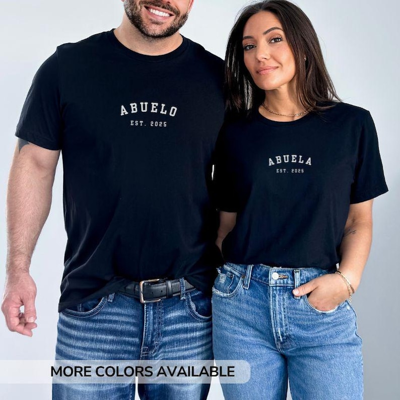 May include: A couple wearing black t-shirts with white text. The man's shirt says "Abuelo Est. 2025" and the woman's shirt says "Abuela Est. 2025". They are both wearing blue jeans.