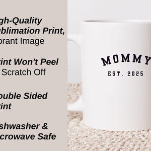 May include: White ceramic mug with a black print that says "MOMMY EST. 2025". The mug is on a beige surface. The text on the mug is in a bold, sans-serif font. The mug is dishwasher and microwave safe.