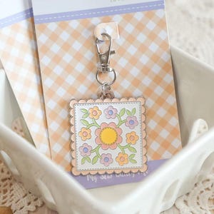 May include: A square zipper charm with a floral design in pastel colors, attached to a silver clasp. The charm is on a card with the text "Pastel Prairie ZIPPER CHARM" and a gingham pattern.