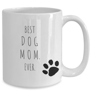 May include: White ceramic coffee mug with black text that reads "Best Dog Mom Ever." A black paw print is to the right of the text.