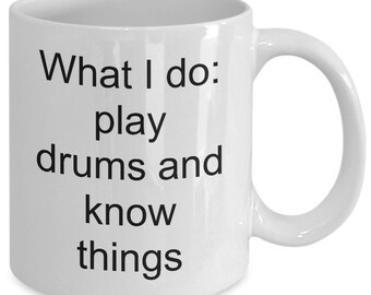 May include: White ceramic coffee mug with black text that reads "What I do: play drums and know things".