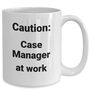 Op de afbeelding: Witte keramische koffiemok met zwarte tekst die "Let op: Case Manager aan het werk" luidt.