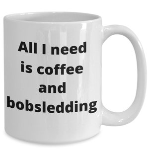 Puede incluir: Taza de café de cerámica blanca con texto negro que dice "Todo lo que necesito es café y bobsleigh."