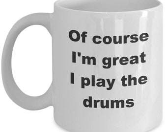 May include: White ceramic coffee mug with black text that reads "Of course I'm great I play the drums".