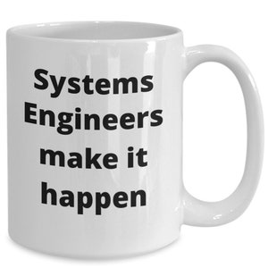 Könnte beinhalten: Eine weiße Keramik-Kaffeetasse mit schwarzem Text, der "Systems Engineers make it happen" lautet.