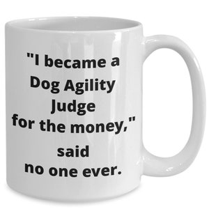 May include: White ceramic coffee mug with black text that reads "I became a Dog Agility Judge for the money," said no one ever."