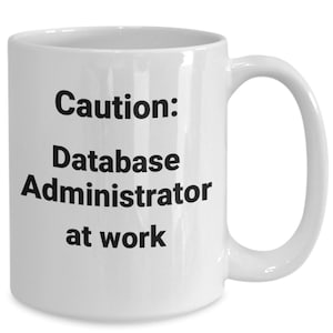 Könnte beinhalten: Weiße Keramik-Kaffeetasse mit schwarzem Text, der "Vorsicht: Datenbankadministrator am Werk" lautet.