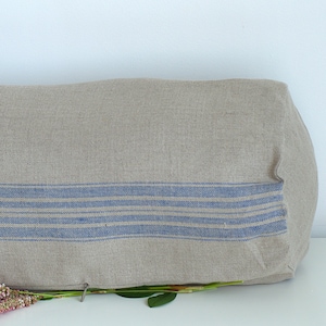 Peut inclure: Un grand coussin cylindrique avec une housse en lin naturel et des rayures bleues. Le coussin est posé sur une surface blanche avec une brindille de fleurs roses.