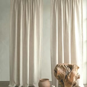 Op de afbeelding: Twee beige gestreepte gordijnen hangen aan een houten roede. Een grote, getextureerde houten sculptuur en twee keramische vazen staan voor de gordijnen. Een kleine witte vaas en een gevlochten touw cirkel zijn ook in de scène.