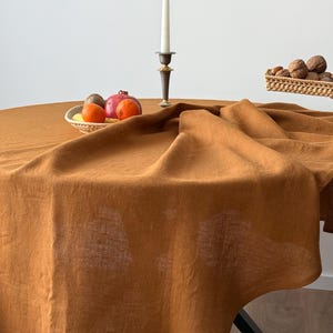 Könnte beinhalten: Eine braune Tischdecke aus Leinen, die über einen runden Tisch gelegt wird. Die Tischdecke hat ein natürliches, rustikales Aussehen und ist perfekt für ein zwangloses Esszimmer.