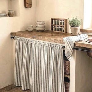 Puede incluir: Una encimera de cocina rústica con superficie de madera y cortina a rayas. La encimera exhibe cuencos, botes de especias y una planta en maceta. Un instrumento de madera cuelga de la pared, añadiendo un toque vintage.