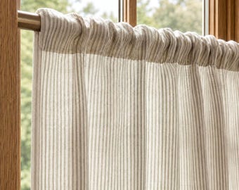 May include: A beige and white striped curtain hanging on a metallic rod. The fabric features a vertical pinstripe pattern with a gathered top section that slides onto the rod, creating soft folds that drape downward across the window frame.