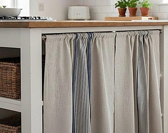 May include: A set of beige linen-look kitchen island curtains featuring vertical navy blue pinstripes. The fabric panels are gathered on a metal rod, covering the open storage area of a white kitchen island with a wooden countertop.