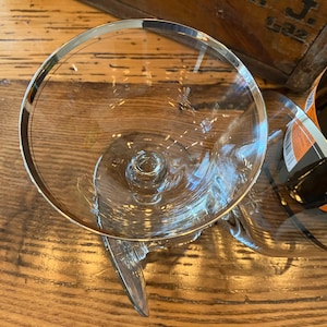 May include: Two clear glass wine glasses with silver rims. The glasses are on a wooden surface.