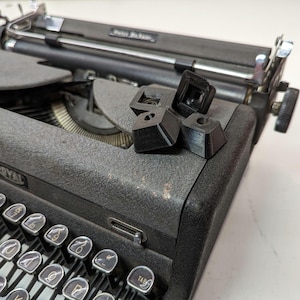 Peut inclure: Une machine à écrire Royal vintage noire avec une touche de tabulation en plastique noir et un ensemble de trois touches en plastique noir sur le dessus de la machine à écrire.