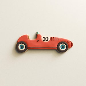 Puede incluir: Cortador de galletas con forma de coche de carreras rojo con detalles en blanco y negro, incluido el número 33. El cortador tiene ruedas azules y blancas y está sobre un fondo blanco liso. El logotipo de "the cookie cutter lab" está en la esquina inferior izquierda.