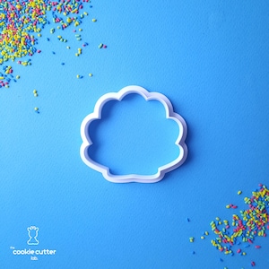 Peut inclure: Emporte-pièce en plastique blanc en forme de nuage sur fond bleu. Le découpoir a un bord festonné. Des vermicelles colorés sont dispersés autour du découpoir. Le logo "the cookie cutter lab" est dans le coin inférieur gauche.