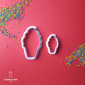 Könnte beinhalten: Zwei weiße Ausstecher in Form von Eiswaffeln auf rotem Hintergrund, mit bunten Streuseln verstreut. Der größere Ausstecher ist etwa 10 cm hoch, und der kleinere etwa 5 cm hoch. Das Logo von Cookie Cutter Lab befindet sich unten links.