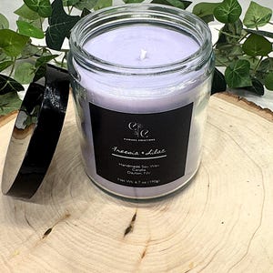 Peut inclure: Une bougie en pot de verre avec de la cire violet clair et un couvercle noir. L'étiquette indique "Freesia & Lilac" et "Handmade Soy Wax". Le poids net est de 190g. Un article de décoration.