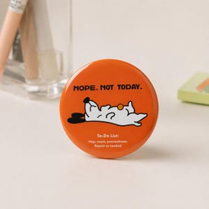 Puede incluir: Botón redondo naranja con el texto "NOPE. NOT TODAY." y una ilustración de un perro de dibujos animados. El perro es blanco con orejas negras y una nariz negra. Debajo, el texto "To-Do List: Nap, snack, procrastinate. Repeat as needed."