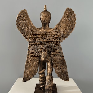 May include: A bronze winged statue of a figure with a snake wrapped around its legs. The statue is standing on a square base.