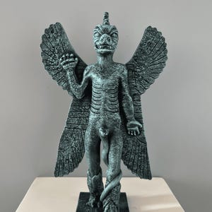 May include: A green, winged, humanoid statue with a snake wrapped around its legs. The statue has a reptilian head with a pointed horn on top. The statue is standing on a square base.