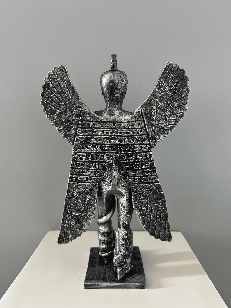 May include: A silver-colored statue of a winged figure with a snake wrapped around its leg. The figure is standing on a square base.