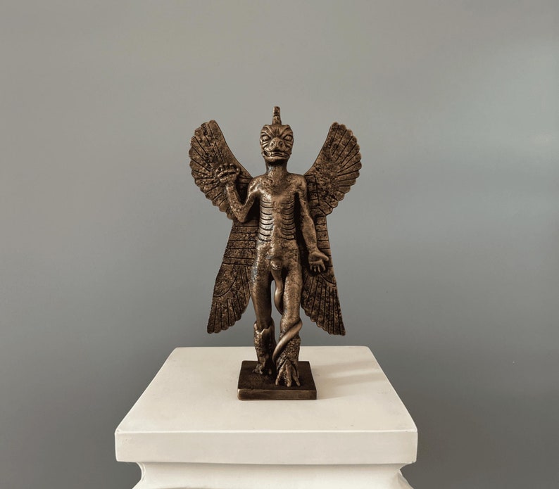 May include: A bronze statue of a winged demon with a snake wrapped around its legs. The demon has a human-like body with wings and a reptilian head. The statue is standing on a white pedestal.