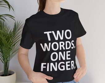 Puede incluir: Una camiseta negra de manga corta con el texto blanco "TWO WORDS. ONE FINGER." impreso en una fuente negrita y sin remates en el pecho. La prenda cuenta con un cuello redondo clásico y un dobladillo recto, ofreciendo un diseño sencillo.
